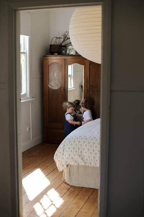 Ein Schlafzimmer mit einem Holzschrank, einem Bett mit floralem Überwurf und einem Fenster für natürliches Licht.