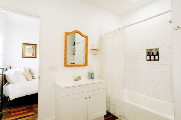 A bathroom with a white sink, a mirror with an orange frame, a shower curtain, and a white bathtub.