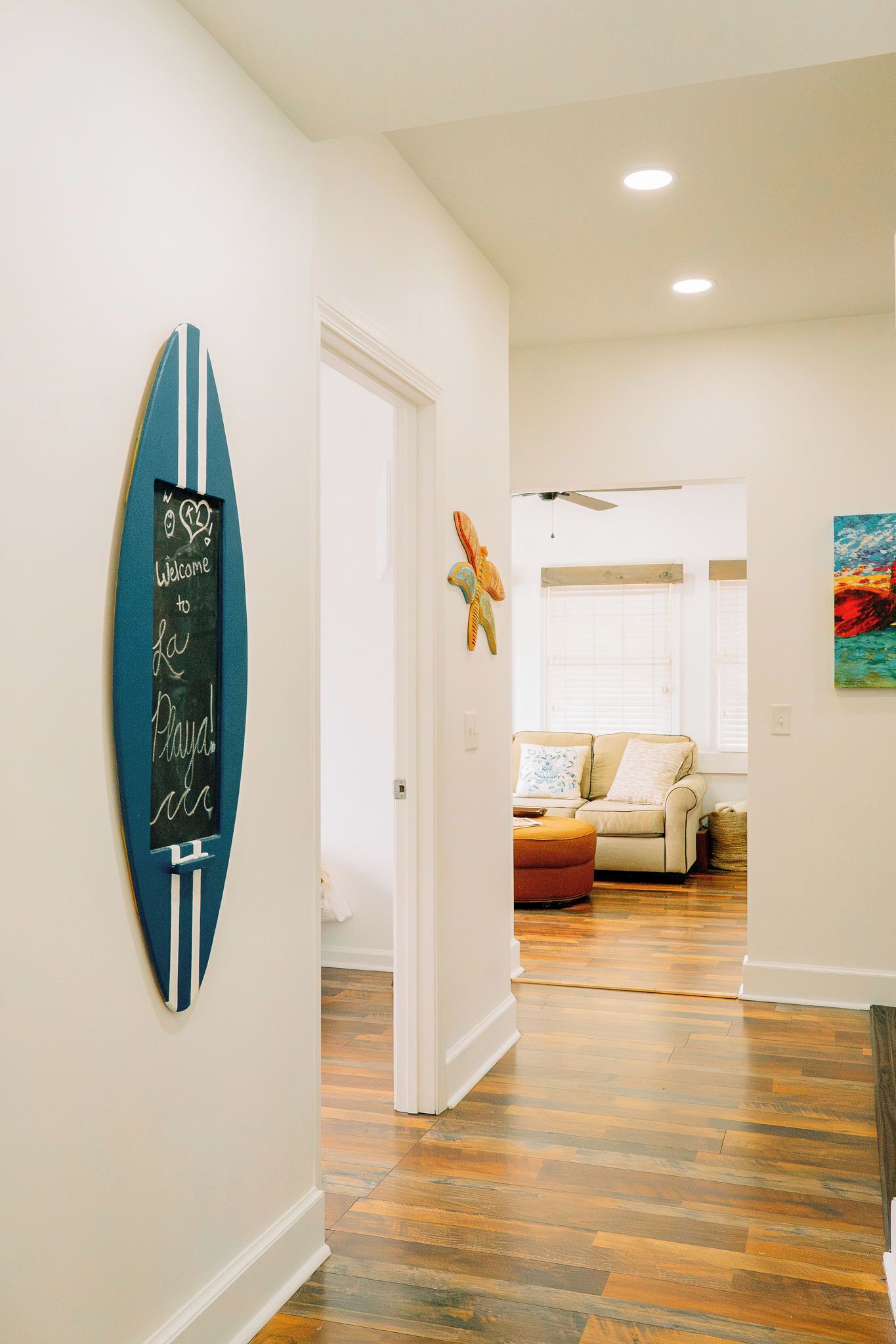 Un couloir avec un panneau représentant une planche de surf, un ventilateur de plafond et un canapé à l’arrière-plan.