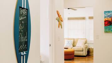 Un couloir avec un panneau représentant une planche de surf, un ventilateur de plafond et un canapé à l’arrière-plan.