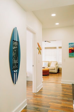 Un couloir avec un panneau représentant une planche de surf, un ventilateur de plafond et un canapé à l’arrière-plan.