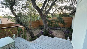 A wooden deck with a view of a backyard featuring a wooden fence, a tree with ivy, and a bird feeder. - Charming 3-bedroom house 20 min. To downtown Austin, 20 min. To Dripping Springs (Austin)