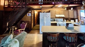 A rustic cabin interior with a kitchen area, wooden staircase, and a dining space with bar stools. - Cozy Cabin in the Woods, Anatone, WA (Anatone)