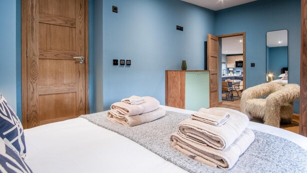 Una camera da letto con un letto grande, un armadio in legno, un bagno con specchio e una piccola cucina sullo sfondo.
