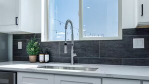 A modern kitchen with a large window, dark backsplash, and white cabinetry. - Kanab Retreat | Hot Tub, EV Charger, Near Zion (Kanab)