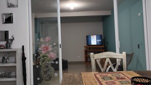 Un soggiorno con un tavolo in legno, una televisione e una porta scorrevole in vetro che dà su un'altra stanza.