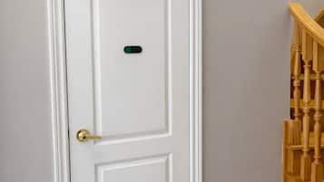 A white door with a gender symbol and a green button, a wooden staircase, and beige tiled flooring.