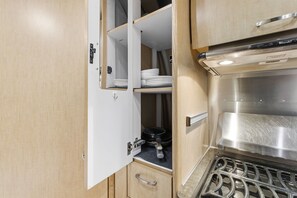 Eine kompakte Küche mit Einbauherd, Spüle und einem Schrank mit Regalen.