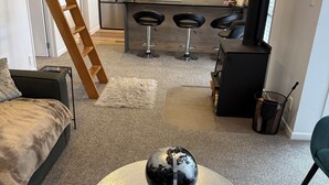 Ett modernt vardagsrum med ett runt bord, en jordglob, en soffa, en stege och ett kök i bakgrunden.