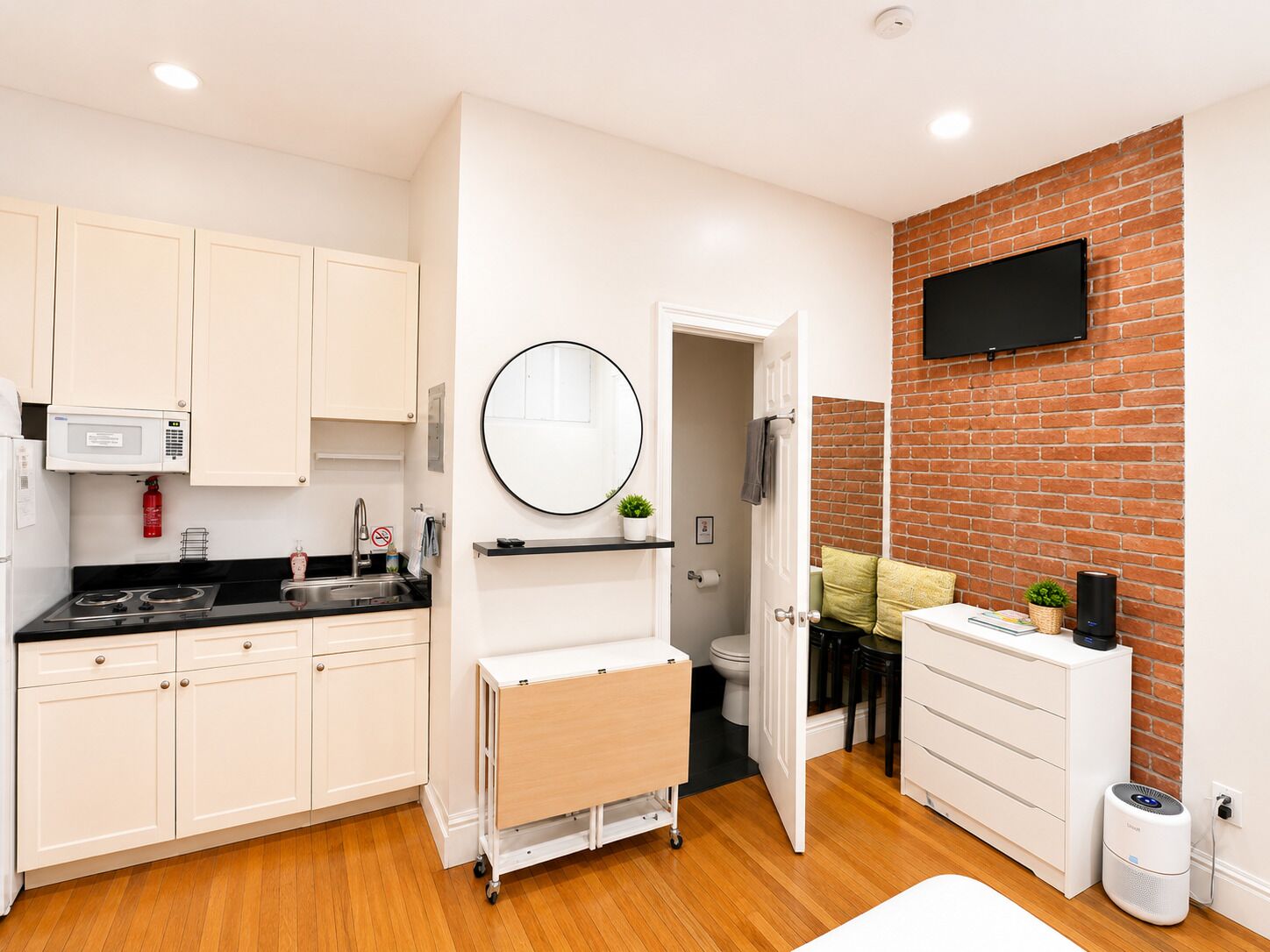 A compact kitchen with white cabinets, a microwave, a sink, and a small cart.