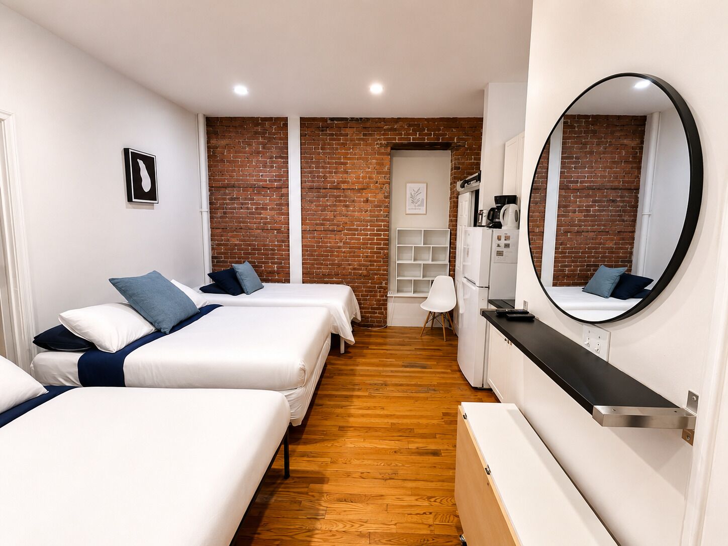 Habitación de hotel con dos camas, una zona de cocina, una pared de ladrillo y un espejo grande.