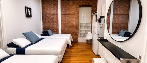 Habitación de hotel con dos camas, una zona de cocina, una pared de ladrillo y un espejo grande.