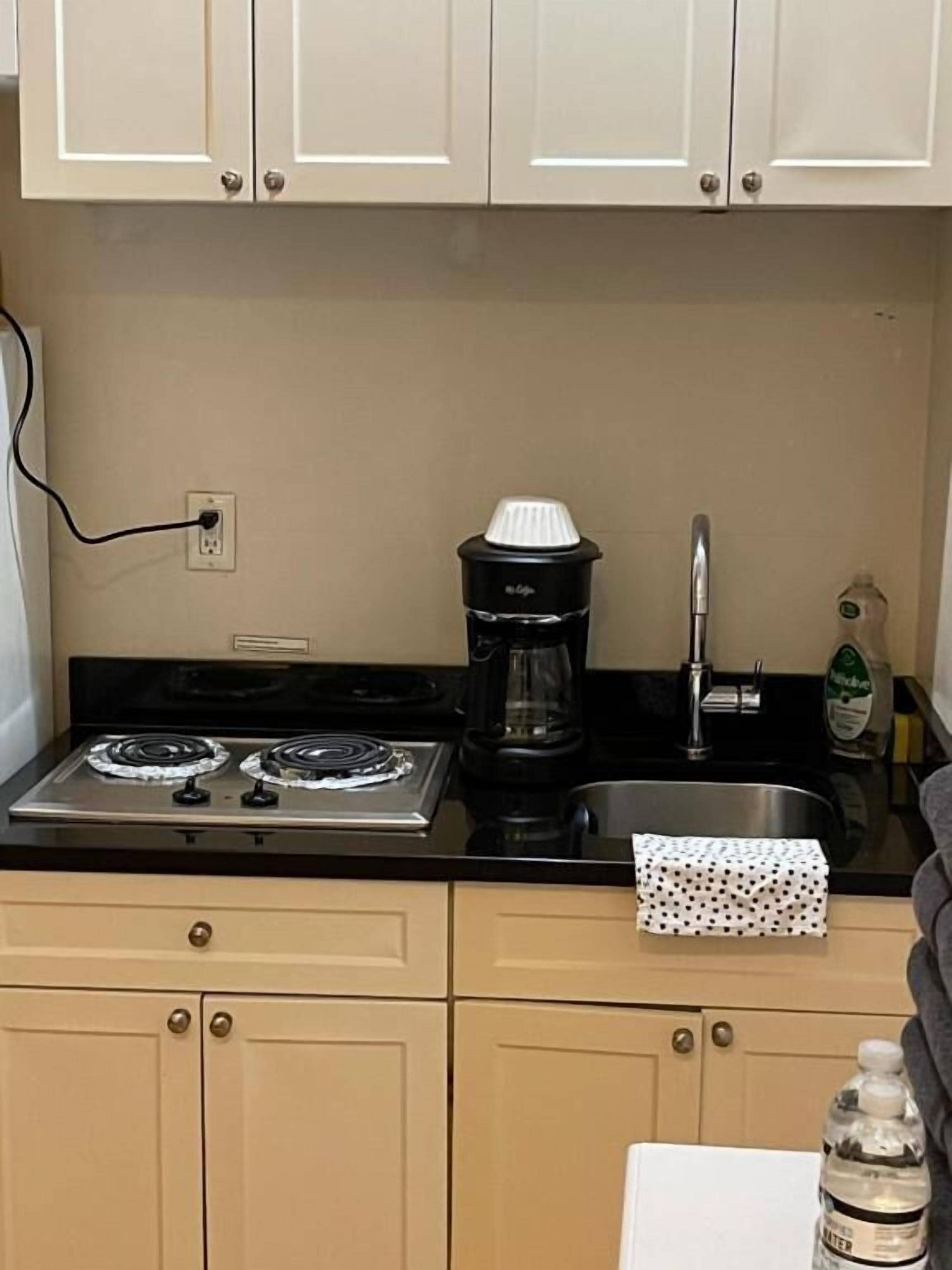 A compact kitchenette with a stove, coffee maker, sink, and a bottle of water.