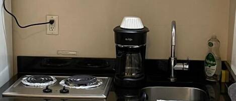 A compact kitchenette with a stove, coffee maker, sink, and a bottle of water.