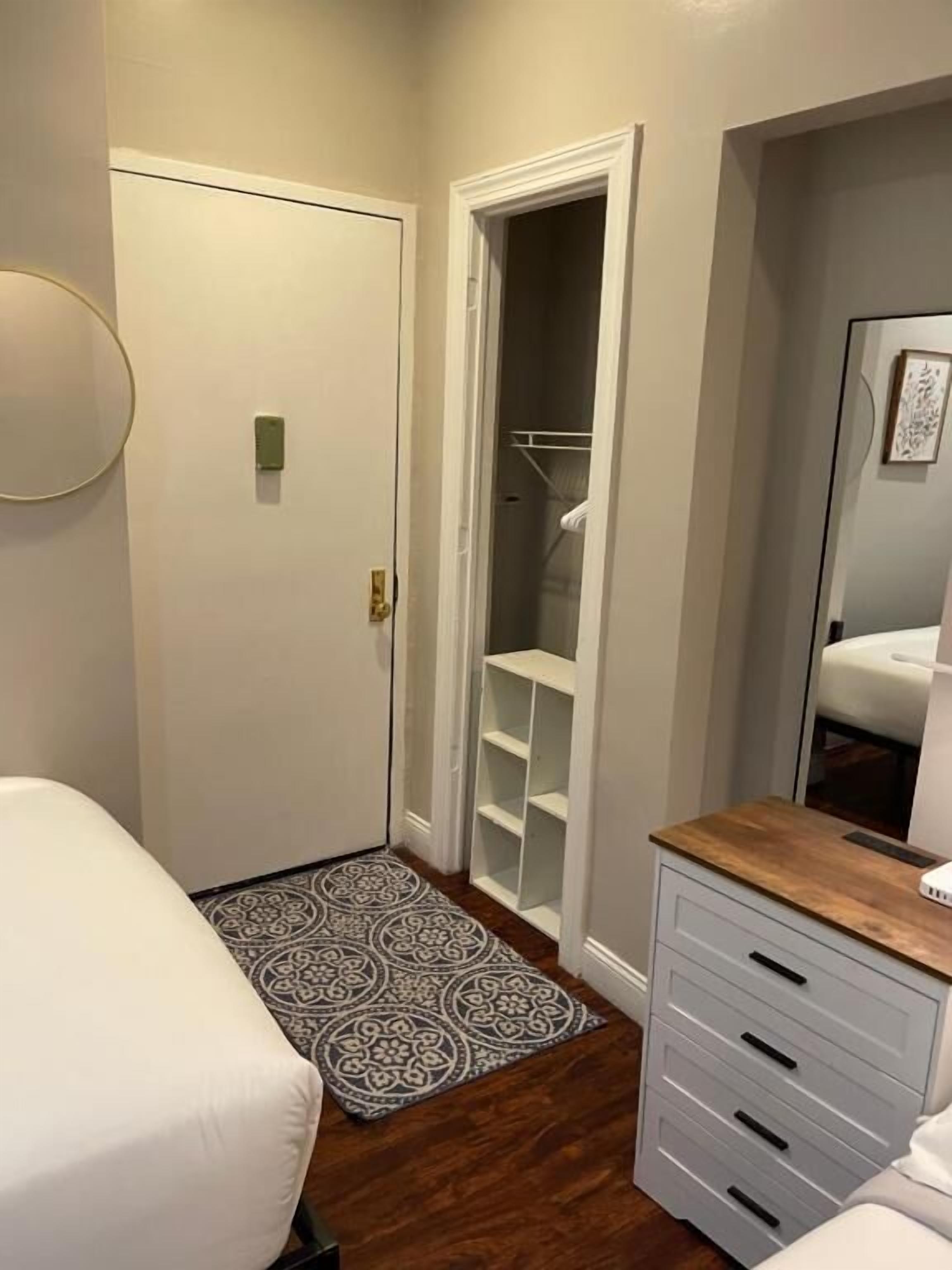 Un dormitorio con cama, mesita de noche, cómoda, armario y alfombra estampada.
