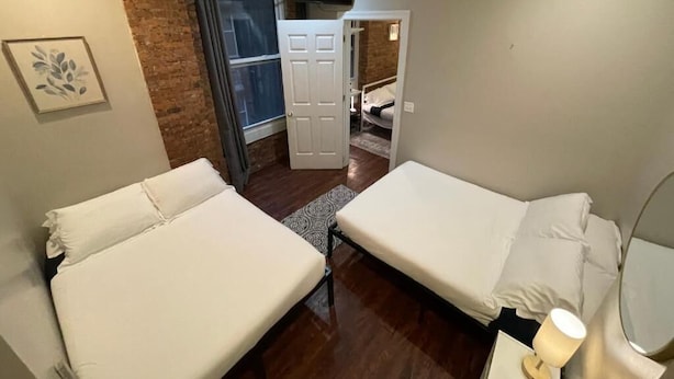 A compact room with two beds, a brick wall, a television, and a door leading to another room. - Nest Aparthotel Manhattan  (New York)