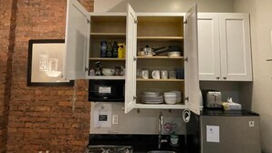 A kitchen with open cabinets displaying dishes, a refrigerator, and a microwave. - Nest Aparthotel Manhattan  (New York)
