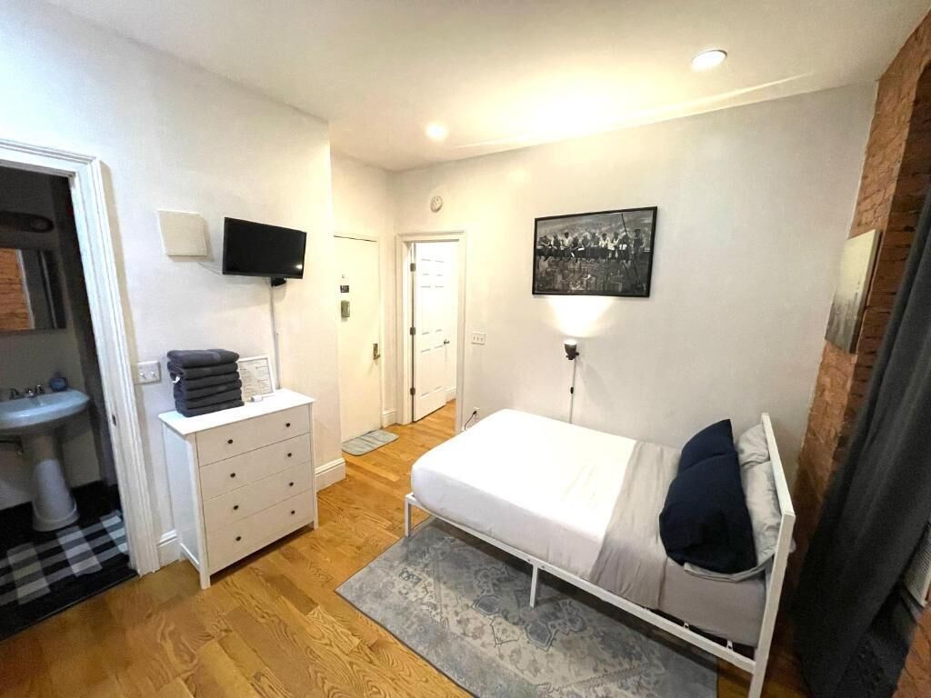 Een slaapkamer met een bed, een dressoir, een televisie, een wandlamp en een deur.