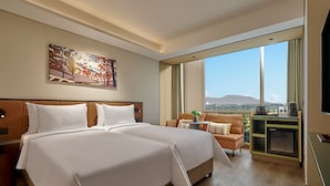 Camera d'albergo con due letti, un divano, un tavolino, una TV e un'ampia finestra con vista sulla città.