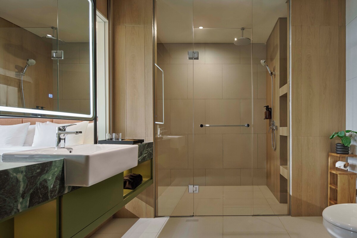 Un baño moderno con ducha de vidrio, tocador de mármol y un espejo grande.