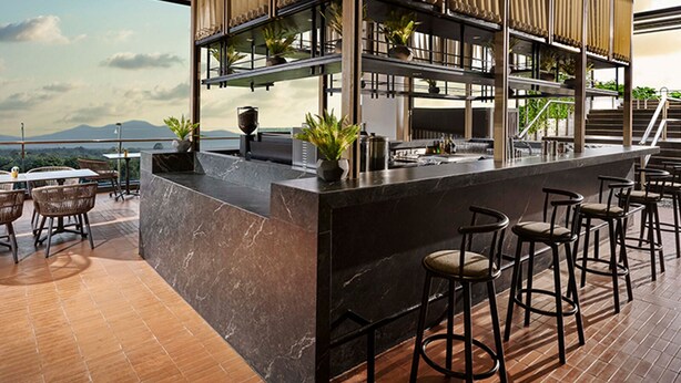 Zona bar moderna con un bancone in marmo, diversi sgabelli e vista sulle montagne.