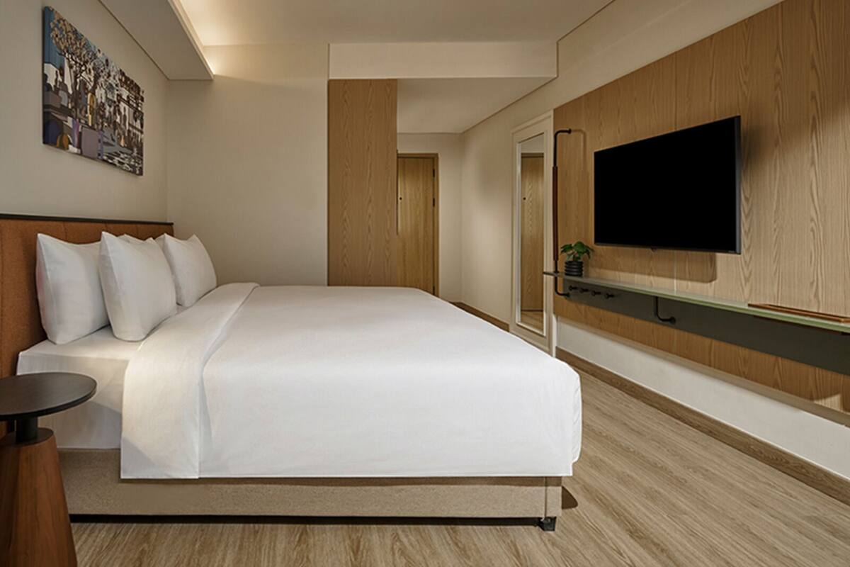 A modern hotel room with a large bed, a flat-screen TV mounted on the wall, and a small table.