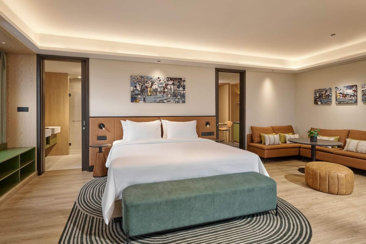 A modern hotel room with a large bed, a sofa, a small table, and a bench.