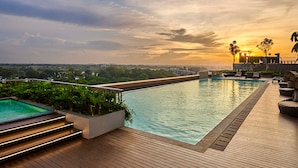 Una piscina a sfioro sul tetto con un solarium in legno, poltrone relax e vista sul tramonto.