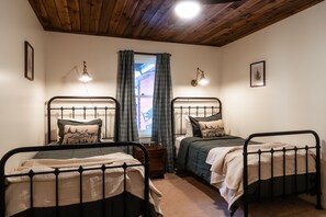 Una stanza con due letti in metallo, soffitto in legno e una finestra con tende.