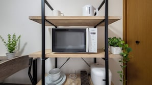 Une cuisine avec un four à micro-ondes posé sur une étagère, une machine à café et une plante en pot.