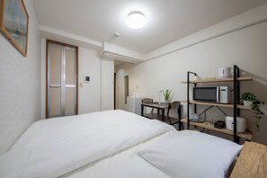 Ett hotellrum med två sängar, ett skrivbord, en stol, en mikrovågsugn, ett litet kylskåp och en hylla med en växt och några föremål.