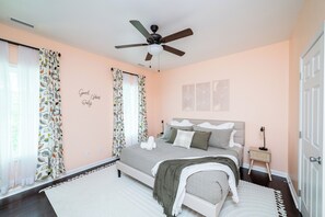 Ein Schlafzimmer mit Bett, Deckenventilator, Nachttisch und einer Wand mit dekorativem Schild.