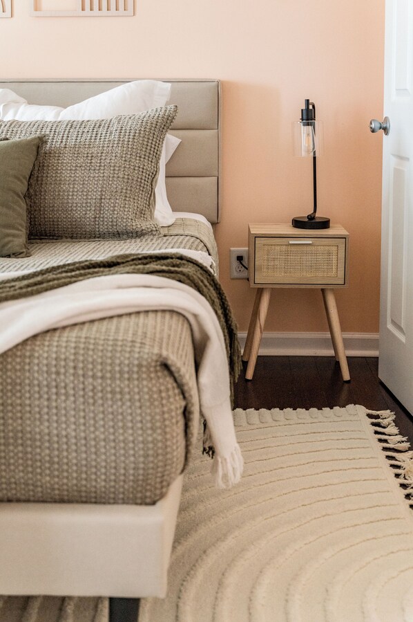 A neatly made bed with a beige headboard, a small bedside table with a lamp, and a white rug on a wooden floor. - 10-Acre Private Retreat Near Liberty, Family-Friendly, Sleeps 14 (Rustburg)