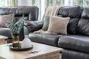 A dark brown leather sofa with a woven throw blanket and a textured pillow. A small white vase with green foliage is on a wooden side table beside the sofa. - 10-Acre Private Retreat Near Liberty, Family-Friendly, Sleeps 14 (Rustburg)