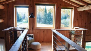 A wooden cabin with a loft bedroom, large windows, a wooden staircase, and a view of a forest. - Secluded Cabin near Lake Vermillion, Sleeps 10, with Hot Tub, and Pet Friendly (Angora)
