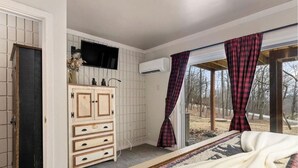 Camera da letto con un letto, una cassettiera in legno, una TV a schermo piatto e una finestra con tende a quadri.