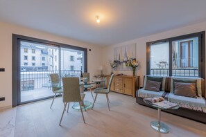 Ein modernes Wohnzimmer mit einem Glastisch, bequemen Sitzmöglichkeiten und Blick auf die Stadt durch große Fenster.