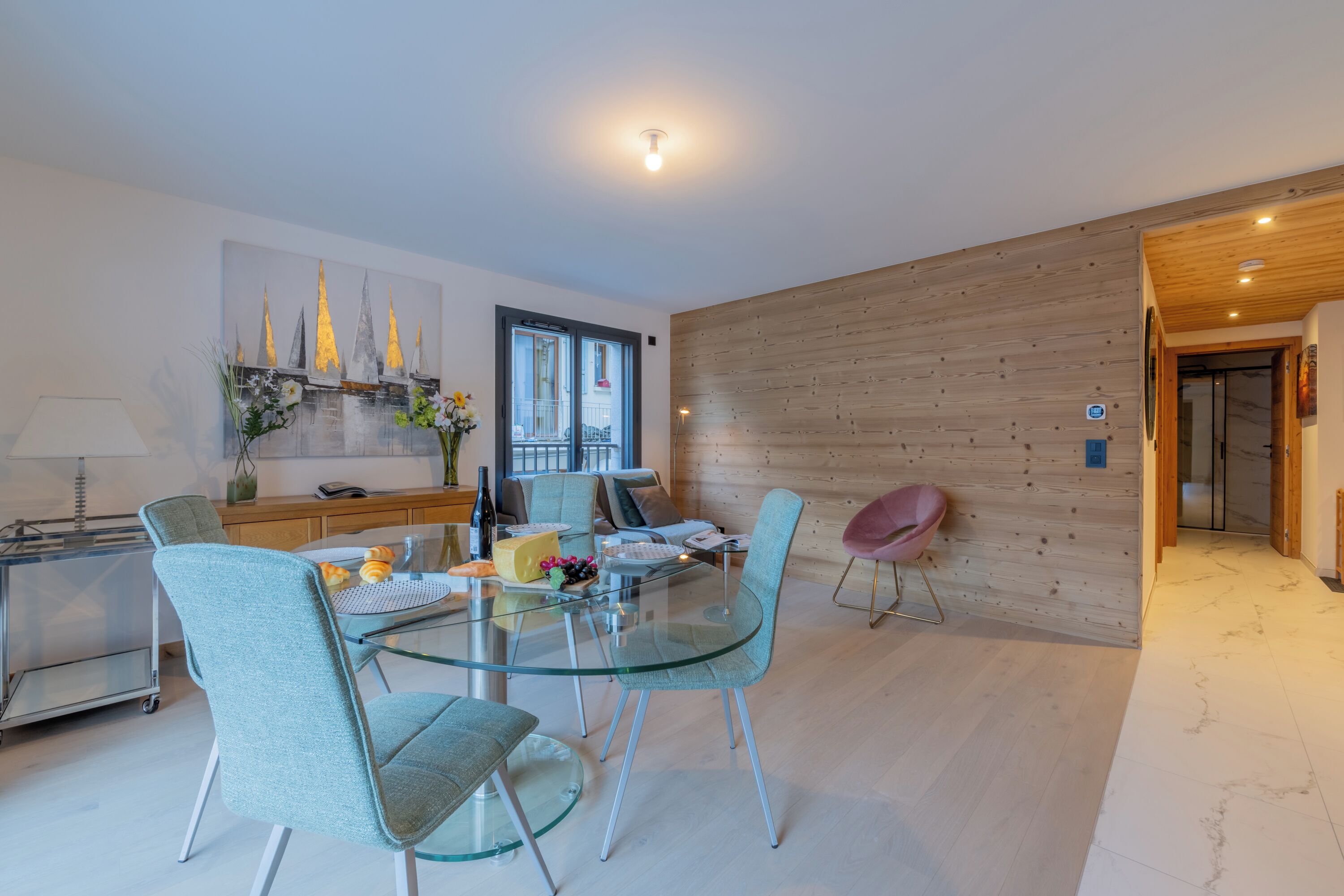 Una cocina moderna con una mesa de comedor de vidrio, sillas azul claro y una pared de madera.