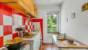 Een keuken met rode en witte tegels, houten kastjes, een eethoek met een tafel en stoelen, en uitzicht op groen via een raam.