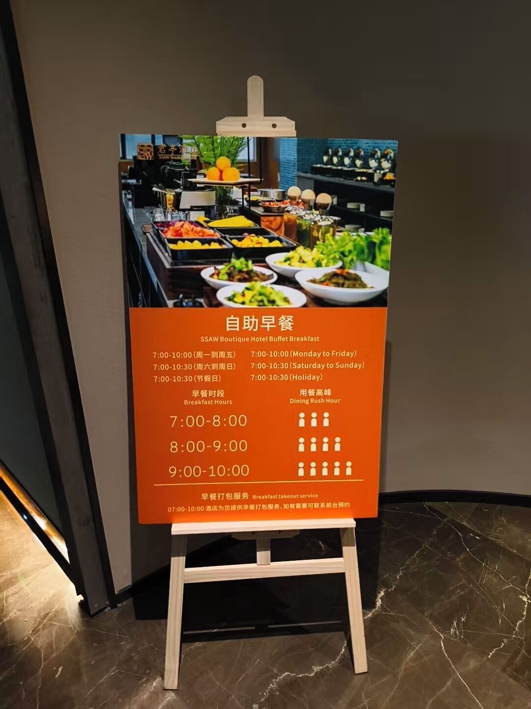 En skylt vid hotellbuffén som visar frukostens öppettider och en indikator för när det är som mest folk i matsalen.