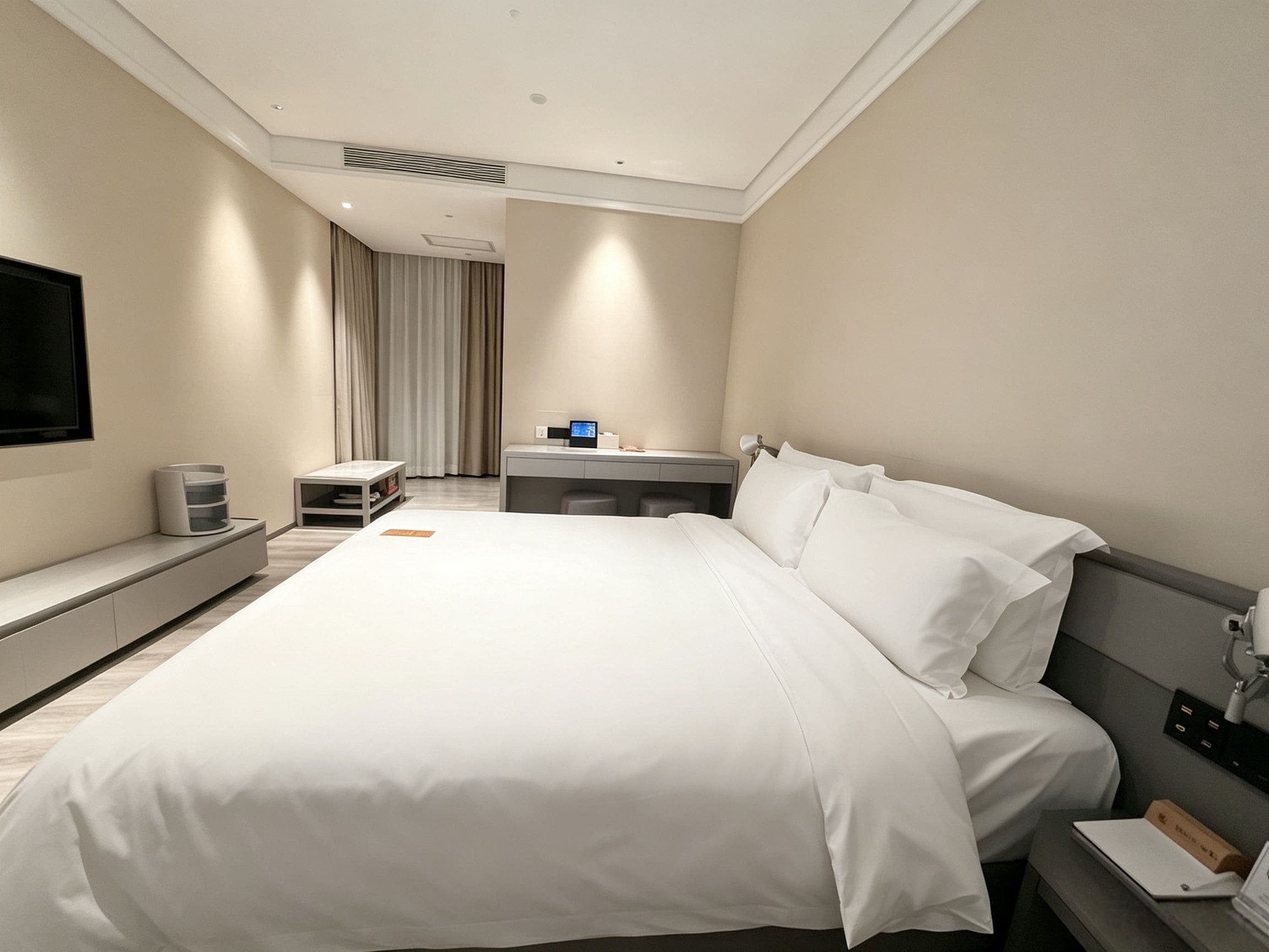 Een hotelkamer met een groot bed, een nachtkastje, een flatscreen televisie aan de muur en een raam met gordijnen.