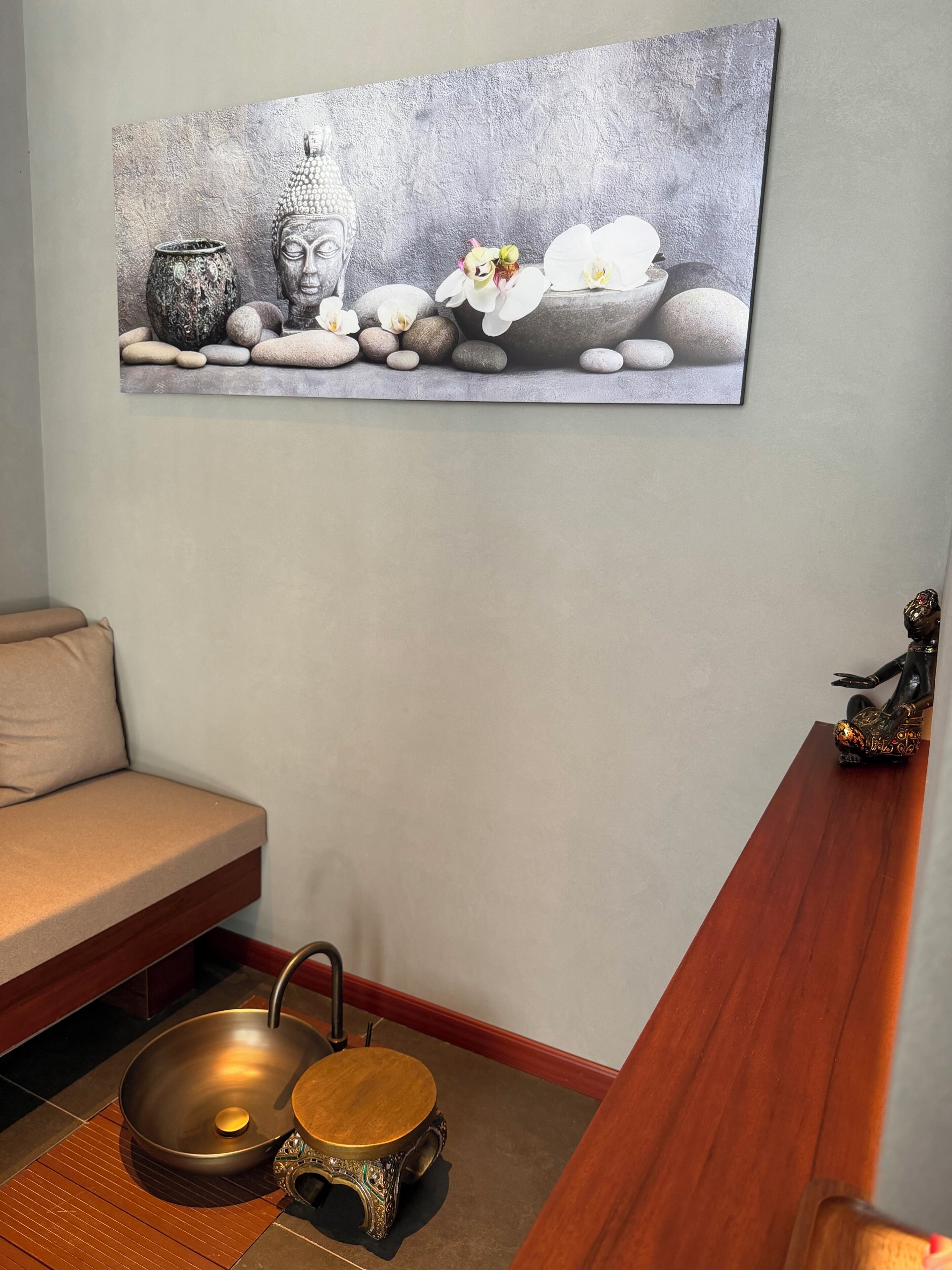 A spa room with a large wall painting, a wooden bench, a sink, and a small statue.