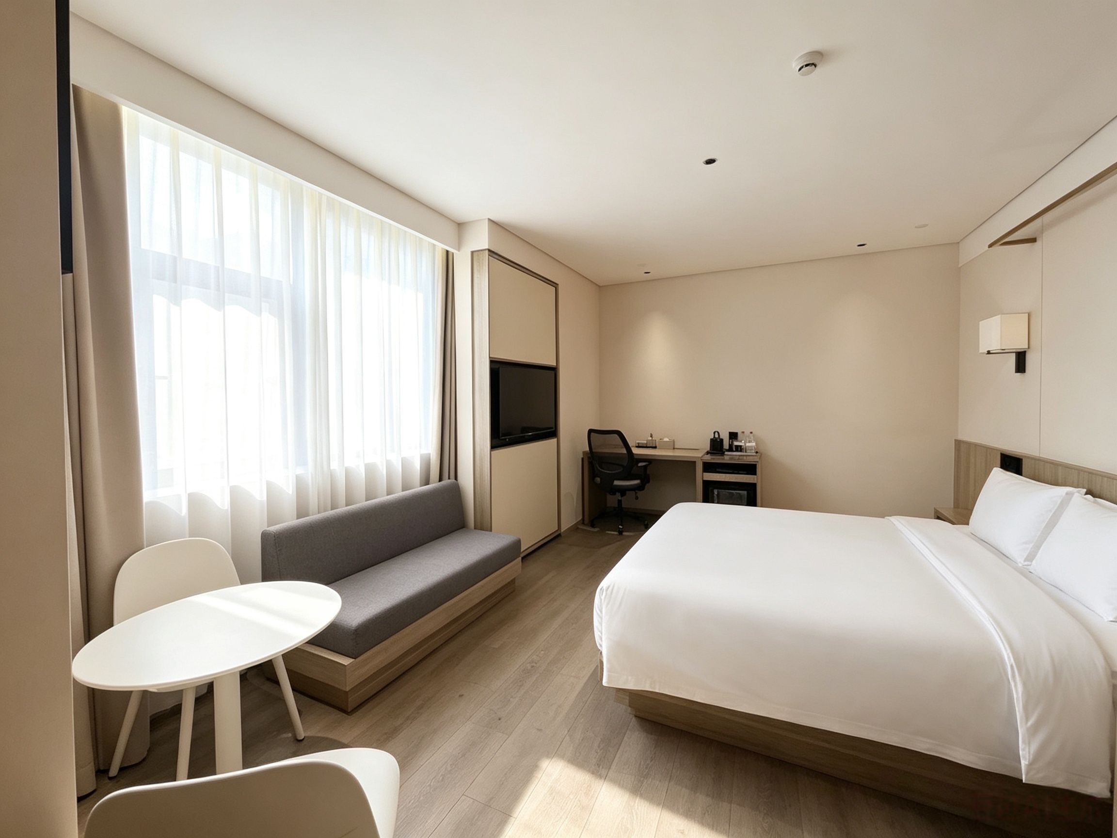 Ein Hotelzimmer mit Bett, Schreibtisch, Sessel, Sofa und Fernseher.