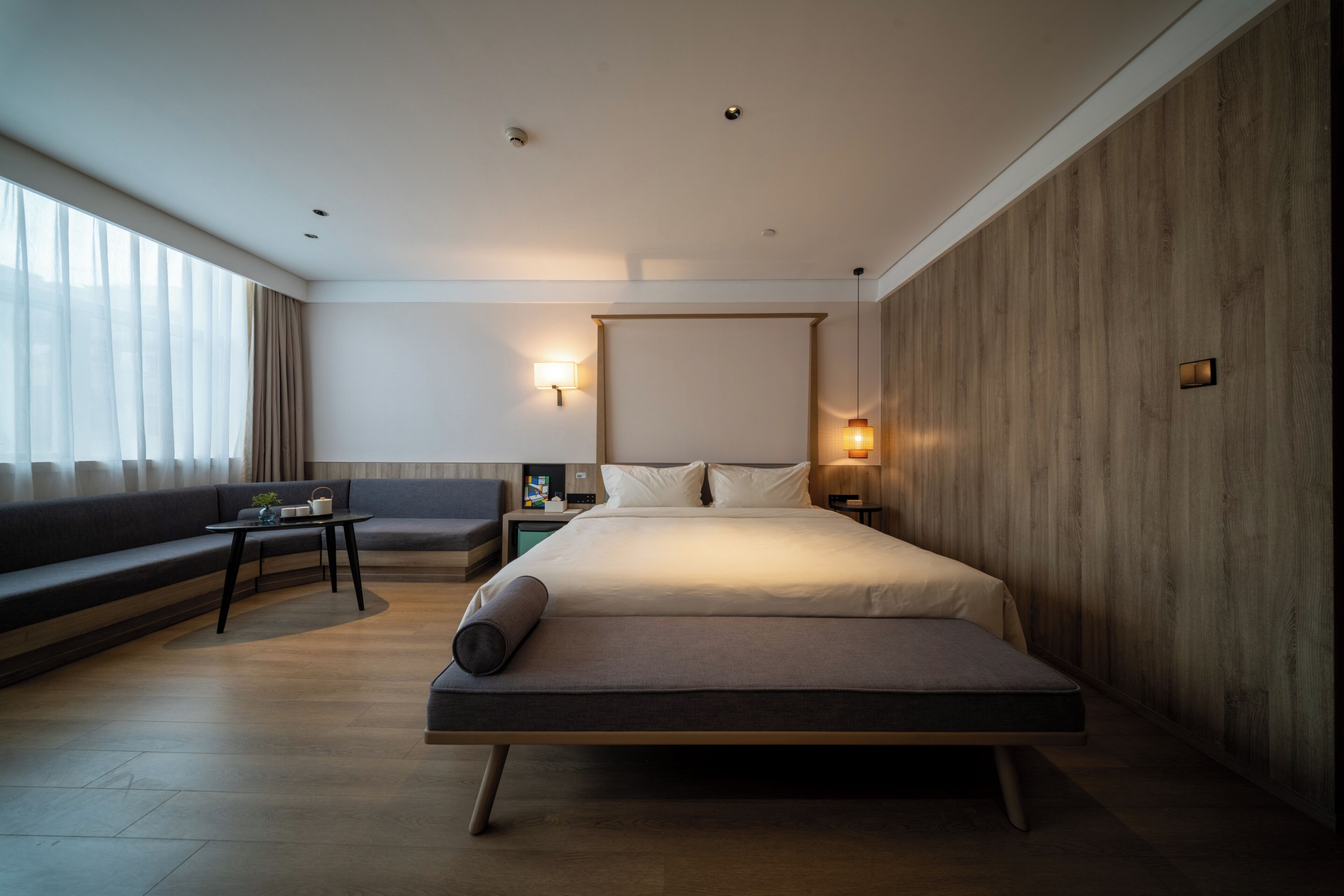 A modern hotel room with a bed, a sofa, a small table, and a nightstand.