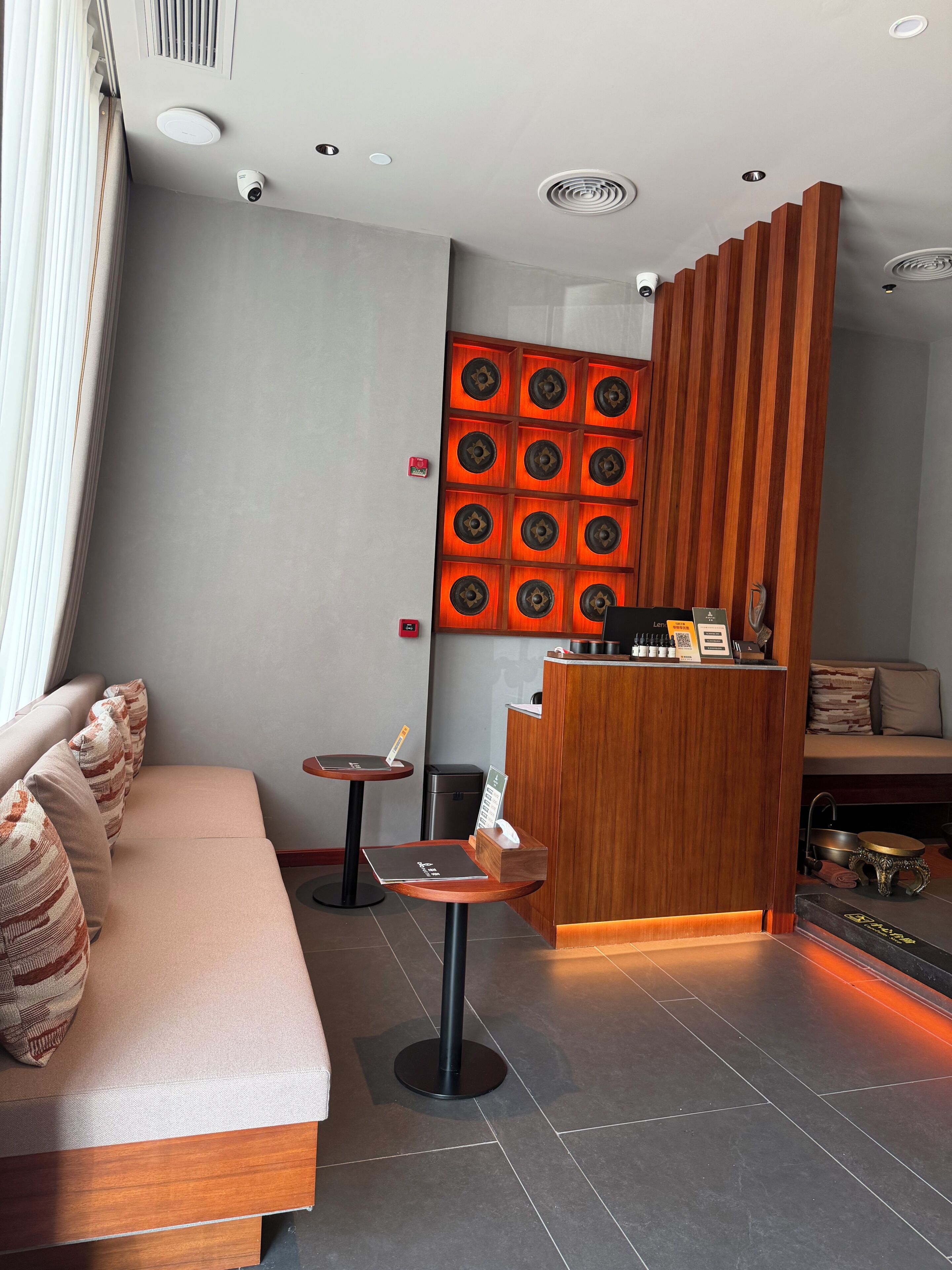 A modern hotel lobby with a reception desk, a sofa with patterned cushions, a small table, and a decorative wall panel.