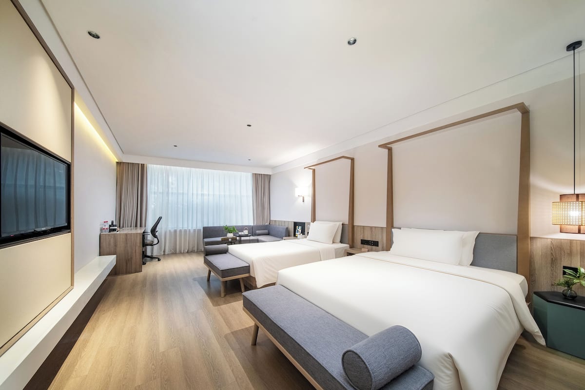 A modern hotel room with a large bed, a sofa, a desk, and a TV.