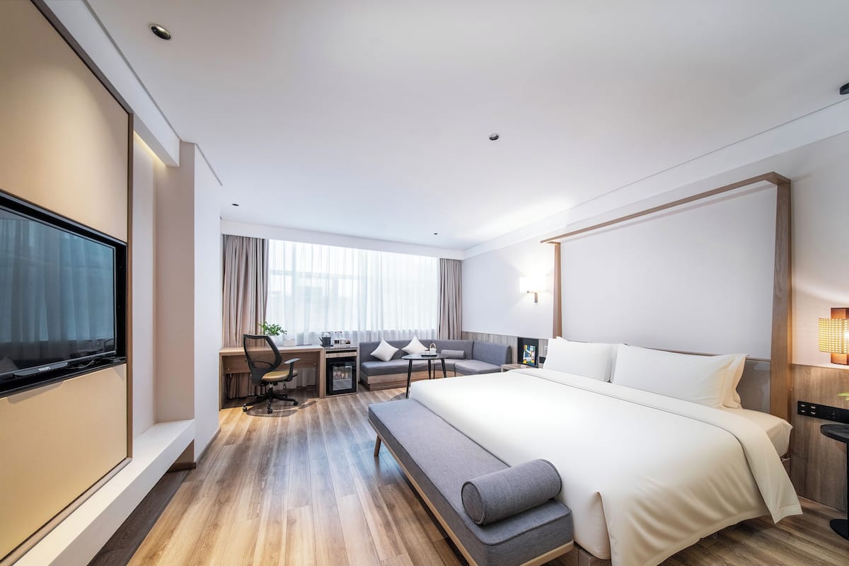 A modern hotel room with a large bed, a desk, a sofa, and a TV.