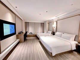 Quarto de hotel com uma cama grande, uma escrivaninha, televisão e janela com cortinas.