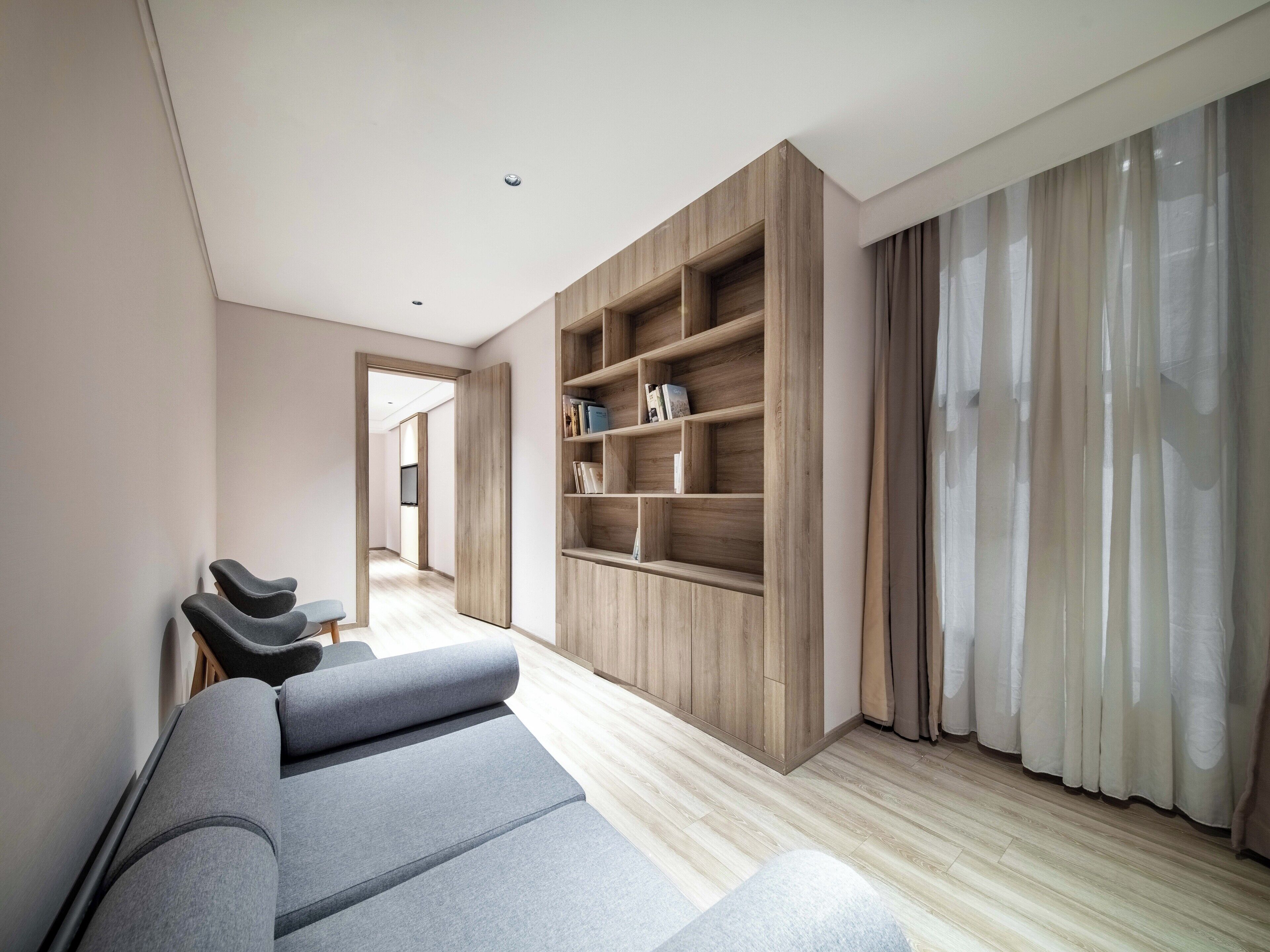A modern living room with a grey sofa, wooden shelving, and a view through a doorway.
