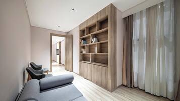 A modern living room with a grey sofa, wooden shelving, and a view through a doorway.
